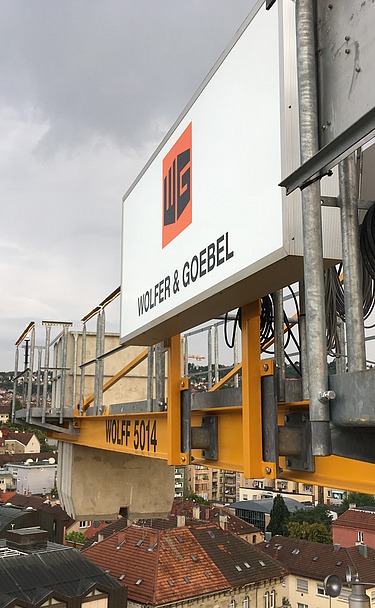 Gelber Baukran mit dem Logo von Wolfer & Goebel über den Dächern von Stuttgart.