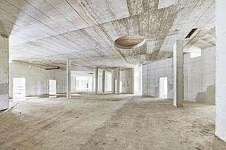 Innenansicht eines Rohbaus mit Betonwänden, Stützen und Decke, große offene Fläche mit runden Deckenaussparungen.