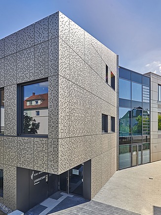 Neubau mit strukturierter Metallfassade und großen Glasflächen in urbaner Umgebung.