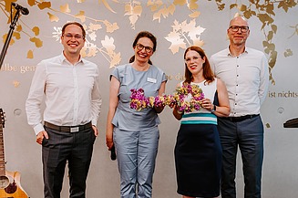 Vier Teilnehmende bei der Eröffnung des Innovation Hub der Evangelischen Heimstiftung. Im Mittelpunkt wird ein bunter Blumenschlüssel als symbolisches Zeichen der Einweihung präsentiert.