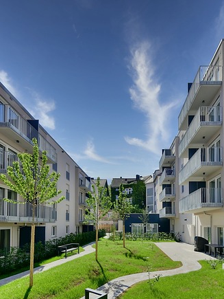 Appartments mit Balkonen und Grünflächen im Innenhof bei sonnigem Wetter.