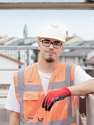 Foto eines gewerblichen Azubis auf der Baustelle, auf dem die Stadt im Hintergrund zu sehen ist
