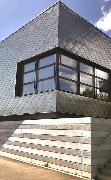 Zeitgemäßes Gebäude mit dunkler Metallfassade, großen Fenstern und seitlicher Treppe unter blauem Himmel