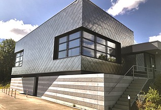 Zeitgemäßes Gebäude mit dunkler Metallfassade, großen Fenstern und seitlicher Treppe unter blauem Himmel