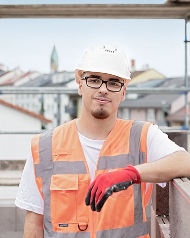 Auszubildender mit Schutzhelm und Warnweste auf einer Baustelle im Rohbau