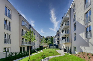 Neue Wohngebäude mit hellen Fassaden, Balkonen und grünem Innenhof unter blauem Himmel.