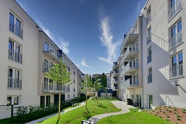 Neue Wohngebäude mit hellen Fassaden, Balkonen und grünem Innenhof unter blauem Himmel.