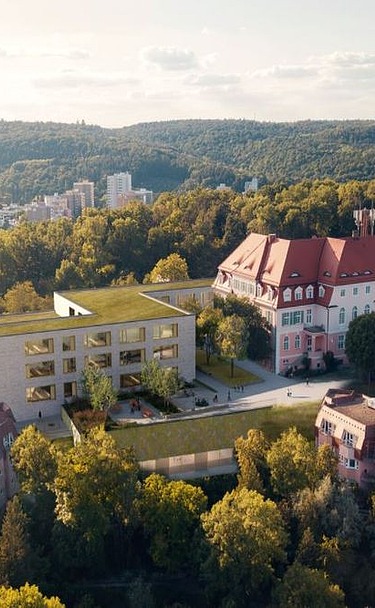 Luftaufnahme eines modernen Schulcampus mit begrüntem Flachdach, umgeben von historischen Gebäuden und Waldlandschaft.