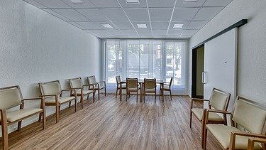 Heller Besprechungsraum mit Holzfußboden, Stühlen und großflächigen Fenstern mit Sichtschutz