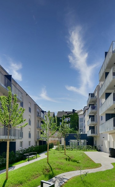 Neue Wohngebäude mit hellen Fassaden, Balkonen und grünem Innenhof unter blauem Himmel.