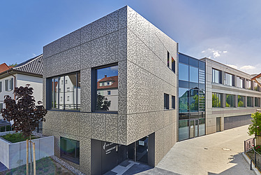 Modernes Landratsamt mit strukturierter Metallfassade und großen Glasfronten, gelegen in einer urbanen Umgebung. Das Verwaltungsgebäude kombiniert zeitgemäße Architektur mit klaren Linien und bietet einen hellen Eingangsbereich.