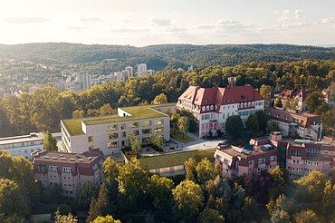 Luftaufnahme eines modernen Schulcampus mit begrüntem Flachdach, umgeben von historischen Gebäuden und Waldlandschaft.