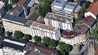 Luftbild von mehreren Wohn- und Bürogebäuden mit begrünten Straßen und Innenhöfen in einer Stadt.
