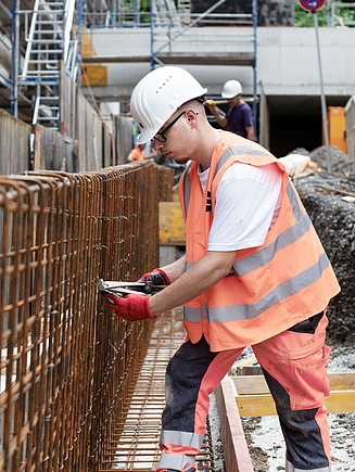 Facharbeiter in Sicherheitsausrüstung montiert Bewehrungsstahl für eine Betonwand