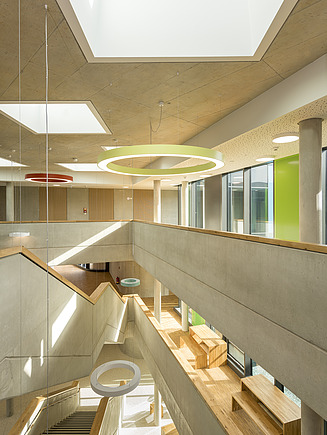 Helle Realschule mit großen Oberlichtern, Sichtbetonwänden und farbigen Designelementen.