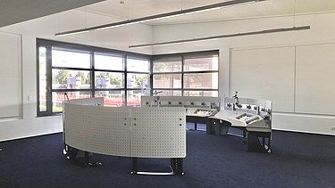 Heller Kontrollraum mit gebogenen Arbeitsstationen, großen Fenstern und moderner Beleuchtung.