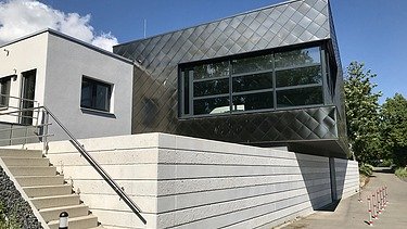 Zeitgemäßes Gebäude mit dunkler Metallfassade, großen Fenstern und seitlicher Treppe unter blauem Himmel.