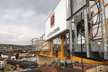 Gelber Baukran mit dem Logo von Wolfer & Goebel über den Dächern von Stuttgart.