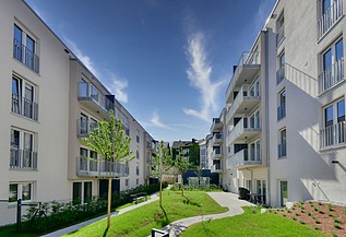 Neue Wohngebäude mit hellen Fassaden, Balkonen und grünem Innenhof unter blauem Himmel.