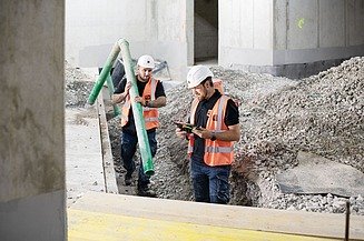Bild von zwei Mitarbeitern mit Schutzausrüstung, die mithilfe des Tablets die Baustelle kontrollieren.
